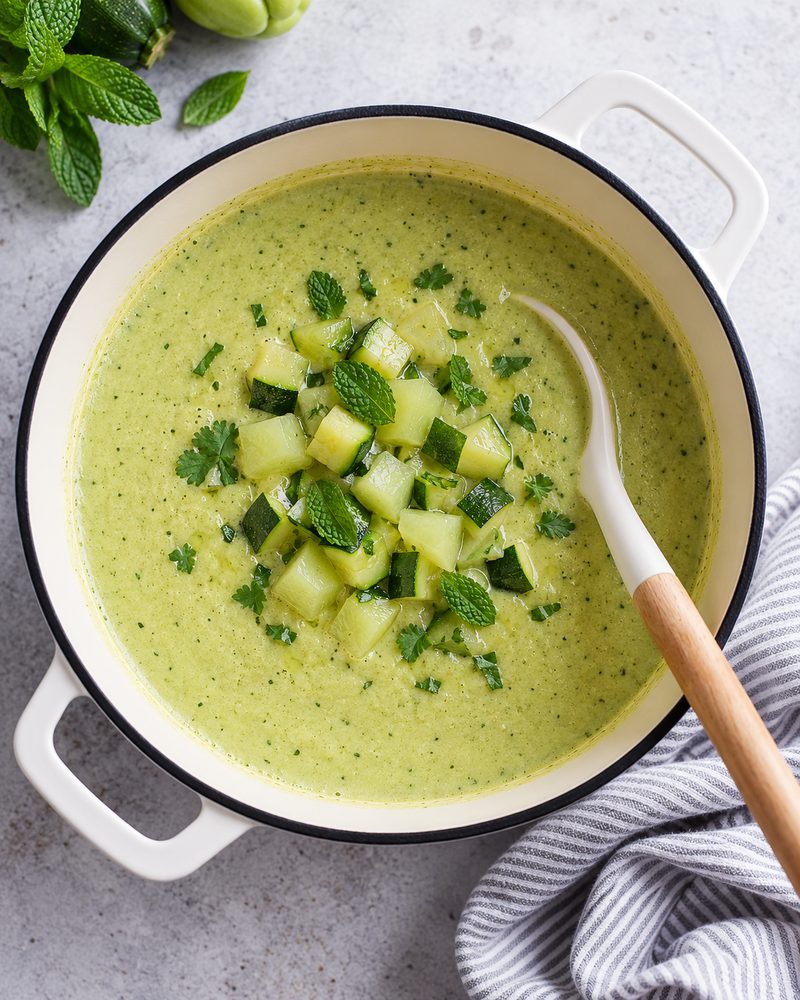 Olla blanca con crema verde clara de chayote y calabacita, cubos de verdura y hojas de hierbabuena encima