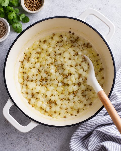 Cebolla picada con comino y semilla de cilantro cocinándose en ghee dentro de una olla blanca