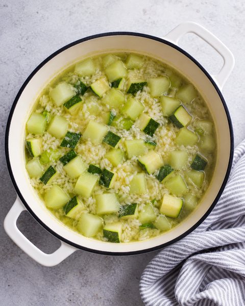 Cubos de chayote y calabacita con arroz cociéndose en agua dentro de la olla