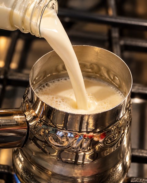 Leche vertiéndose en una olla pequeña de acero sobre la estufa