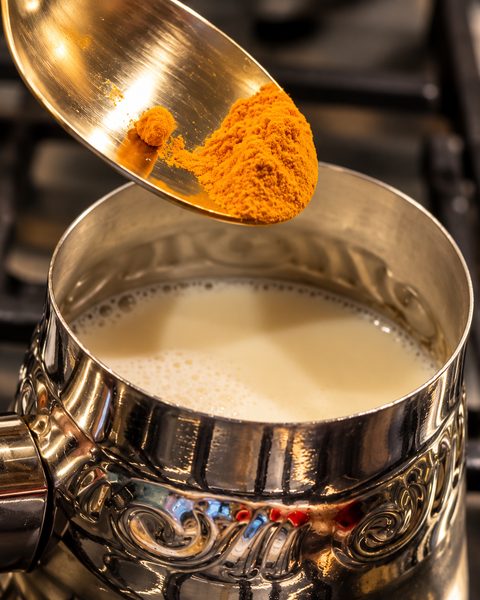 Cuchara con cúrcuma molida a punto de caer en la leche caliente